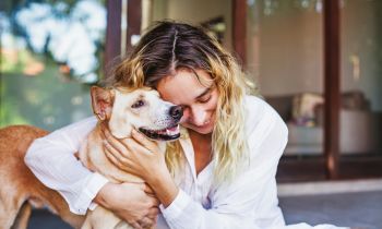 A woman sits on the floor, lovingly hugging her dog